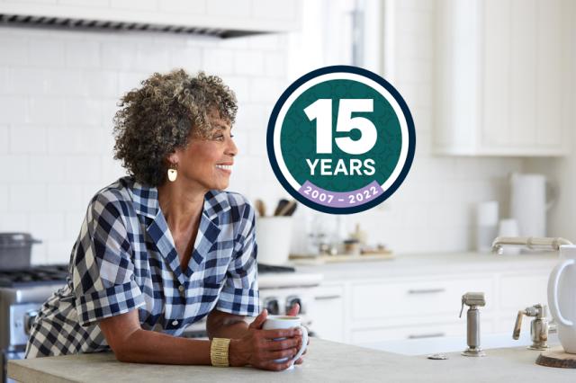 Woman leaning on kitchen counter looking at 15 year logo